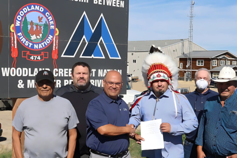 Employees of Mercer and Woodland Cree First Nation stand in front of a large Peace River Logging sign, holding a contract together.