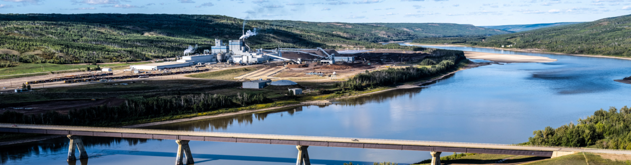 Landscape view of the Mercer Peace River Pulp Mill. In the foreground, a bridge crosses the Peace River.