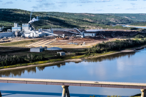 Landscape view of the Mercer Peace River Pulp Mill. In the foreground, a bridge crosses the Peace River.