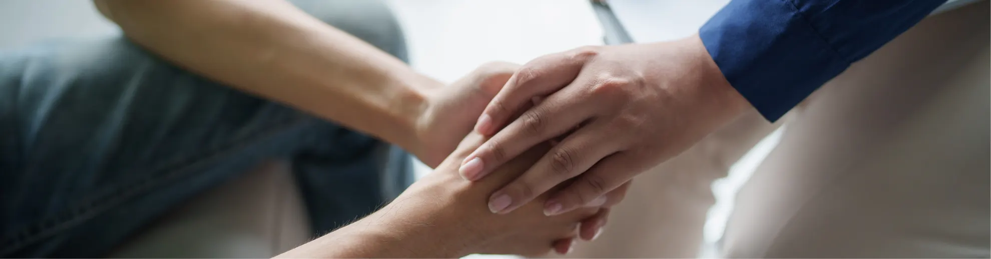 Close-up: A hand in a blue shirt comfortingly holds the hand of a person in dark clothing. Symbolizes support.