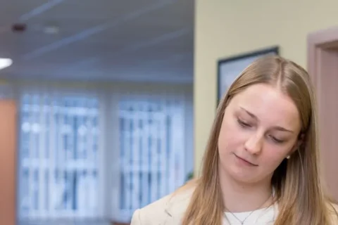 Three people. A young man and a woman are looking intently at something. Another person wearing glasses is looking at the woman. Office environment.